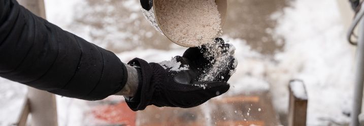 Hand streut Salz auf Schnee.